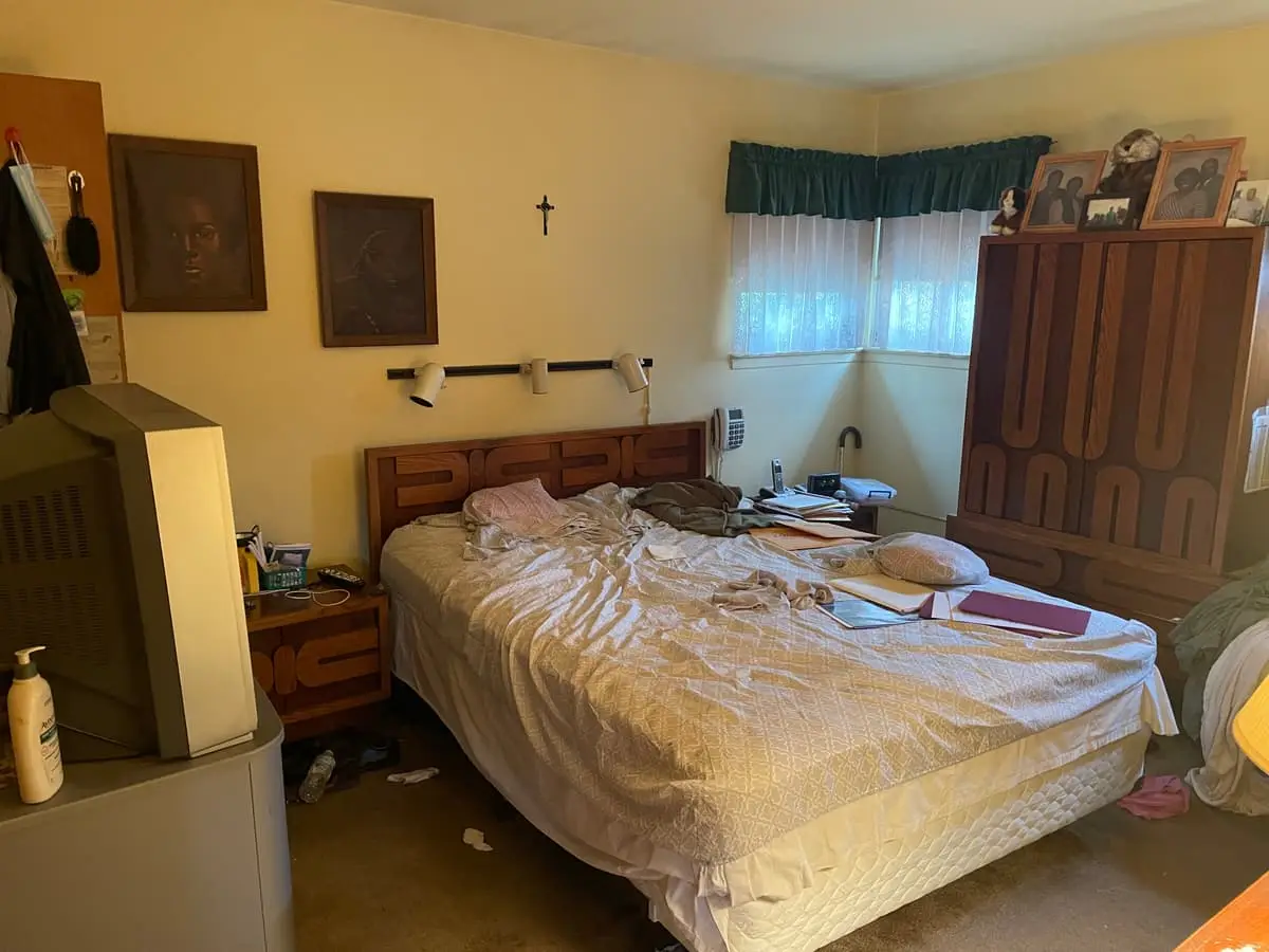 Selling a hoarder house in Babylon: bedroom with an unmade bed and a wood headboard
